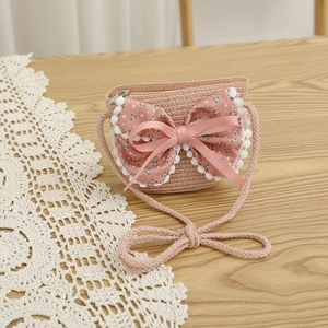 Détail du sac bandoulière en paille rose avec nœud floral et bordure en dentelle