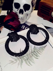 Artistic macro shot of black oversized hoop earrings with dense rhinestones on a skull