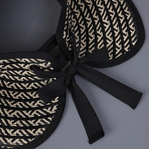 Detail view of woven sun hat with black ribbon bow and metal eyelet texture