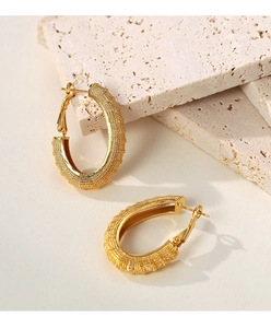 Macro detail of gold U-shaped earrings with grainy texture on light stone surface