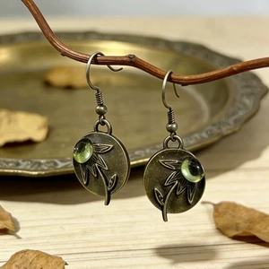 Pendientes vintage de bronce con gemas verde esmeralda en expositor de ramas rústicas