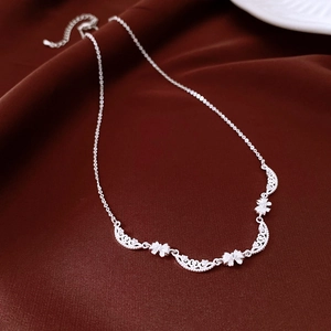 Detailed close-up of a silver bow necklace with floral hollow design on dark velvet