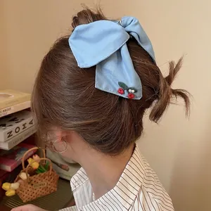 Light blue knit bow hair clip with cherry charm decoration shown on female hair