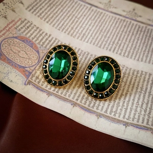 Detailed view of vintage gold earrings with oval green gemstones on antique parchment