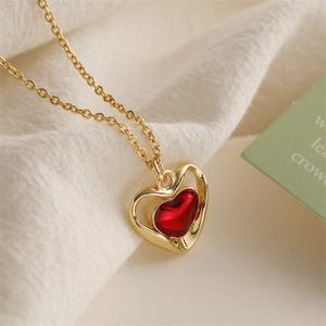 Macro detail of golden necklace with a red heart pendant on soft white fabric background