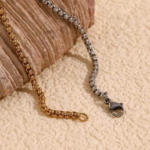 Macro detail of gold and silver box chains with lobster clasps on a natural stone base
