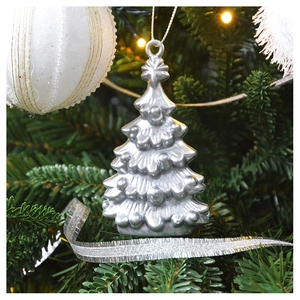 Close-up of a silver Christmas tree ornament hanging on a pine branch with warm lights