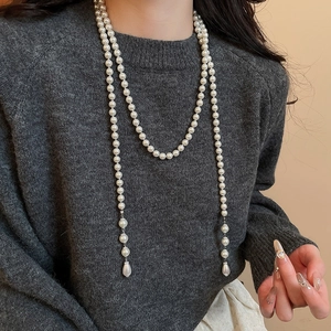 Close-up of double-layered pearl necklace with drop pendant on a grey sweater