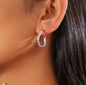 Détail d'une boucle d'oreille créole torsadée argentée portée avec texture métal