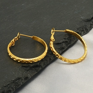 Detailed view of gold stainless steel hoop earrings with textured finish on dark shale