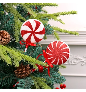 Close-up of red and white glitter Christmas lollipop with bow on a festive green tree