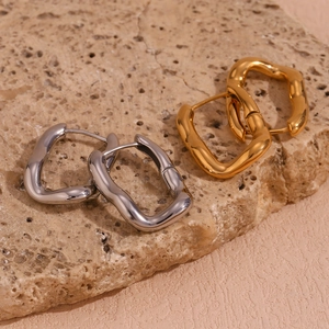 Close-up of gold and silver irregular U-shaped hoop earrings on natural stone background