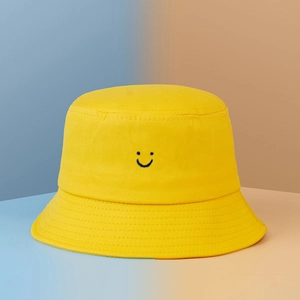 Detail of yellow cotton bucket hat featuring a black embroidered smiley face and stitching
