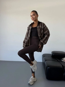 Detail of a casual outfit featuring a brown plaid shirt, dark pants and chunky sneakers