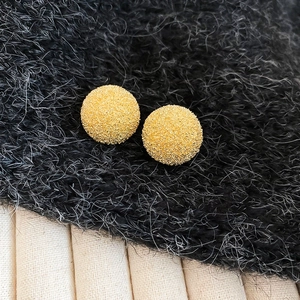 Macro detail of gold round stud earrings featuring a sparkling sandblasted matte texture
