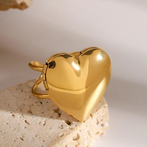 Macro view of a golden heart-shaped locket ring displayed on a natural beige stone