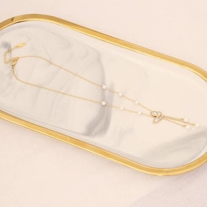 Detail of gold butterfly necklace with pearl accents on white marble jewelry tray