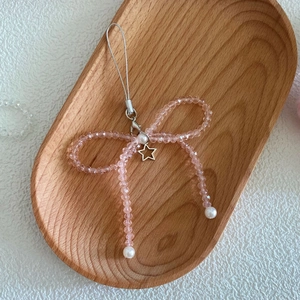 Detailed view of pink crystal beaded bow phone charm on a natural wooden tray background