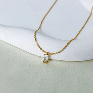 Macro shot of gold necklace featuring a rectangular emerald-cut zircon pendant on white stone