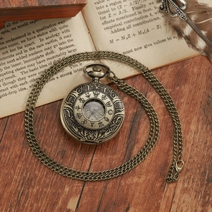 Vintage bronze pocket watch with intricate engravings placed on old book with quill
