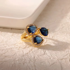 Nahaufnahme eines goldenen Rings mit drei birnenförmigen blauen Steinen und Diamantkranz