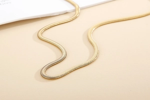 Gros plan d'un collier chaîne serpent dorée plate avec texture lisse sur fond beige