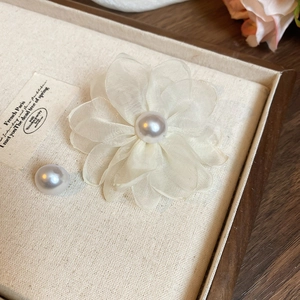Macro view of white fabric flower brooch with pearl center in a wooden jewelry box
