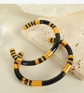 Detail of two gold and black striped open bangles on textured stone background