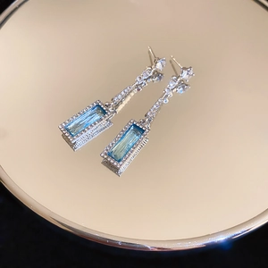 Detail of silver drop earrings featuring a blue rectangular gemstone on a mirror