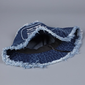 Dettaglio dei bordi sfrangiati e stampa di lettere bianche su un cappello bob in denim blu