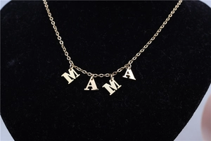 Detailed close-up of golden MAMA letter pendants on a black velvet necklace stand