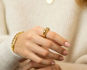 Close-up of polished gold dome ring and textured cuff bracelet on model wearing knitwear