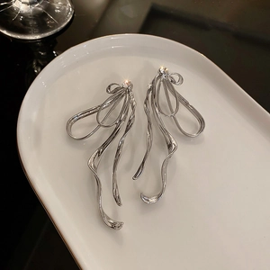 Détail des boucles d'oreilles nœud argenté avec texture métal liquide sur céramique blanche
