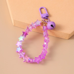 Close-up of purple star-shaped acrylic beads with metal bell keychain on beige stone