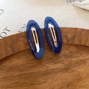 Close-up of blue acetate oval hair clips with gold lettering on a wooden tray