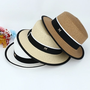 Détail de chapeaux en paille tissée avec rubans noirs et logo métallique M de luxe