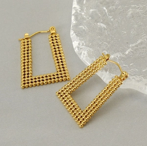 Macro detail of gold U-shaped rectangular earrings with granulated beaded texture
