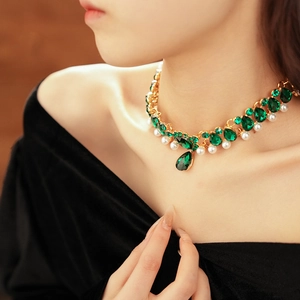 Macro shot of vintage gold necklace with green stones and pearl drop pendant on a model