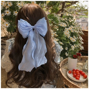 Detail of light blue organza bow hair clip styled on a model in a sunny outdoor setting