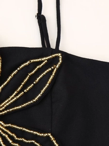 Detailaufnahme des schwarzen Oberteils mit goldenen Perlenverzierungen am Schultergurt