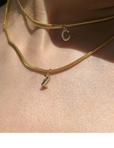 Detail of double-layer gold snake chain featuring a rhinestone letter C pendant and zigzag charm