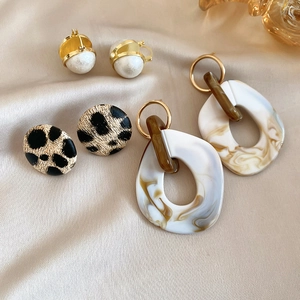 Detail of leopard print studs and marble resin earrings on silk fabric background