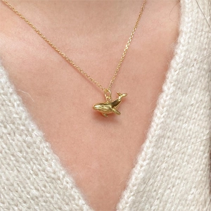 Close-up of a golden whale pendant necklace worn on a white knitted sweater