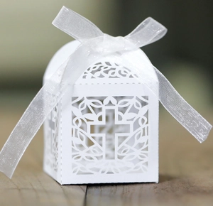 Close-up of white laser-cut cross candy box with elegant white ribbon bow for wedding favor