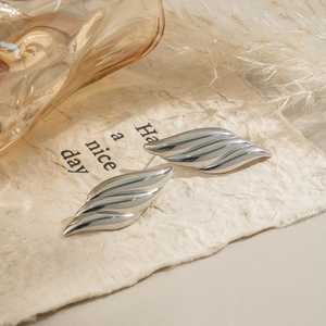 Detail view of silver stainless steel leaf earrings on textured paper with natural lighting