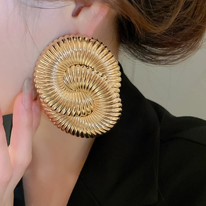 Close-up of a model wearing large golden spiral textured metal geometric stud earrings