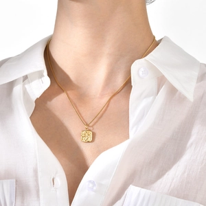 Close-up of golden square embossed pendant on a stainless steel necklace worn by a model