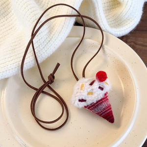 Detail of handmade plush ice cream pendant with red cherry on a brown suede cord