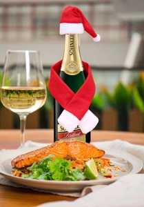 Close-up of a mini red and white plush Christmas hat and scarf set on a wine bottle