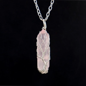 Close-up of pink crystal hexagonal pillar pendant with silver wire tree of life wrap